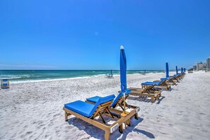 A beach with rows of wooden lounge chairs and blue umbrellas, a clear sky, and the ocean in the background. - Seaside Panama City Beach Condo w/ Outdoor Pool! (Panama City Beach)