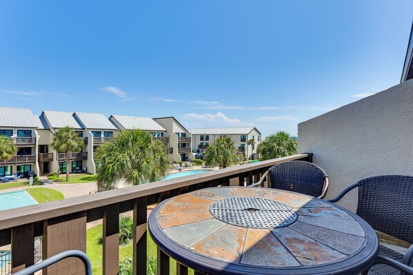 A balcony with a round table and chairs, overlooking a pool and a building with multiple balconies. - Seaside Panama City Beach Condo w/ Outdoor Pool! (Panama City Beach)