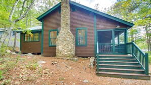 A cabin with a stone chimney, a porch with steps, and a view of the surrounding forest. - Private Island w/ 2 Cottages on Kezar Lake! (Lovell)