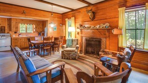 A cozy cabin interior with a dining area, fireplace, and wooden walls. - Private Island w/ 2 Cottages on Kezar Lake! (Lovell)