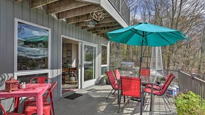 A wooden deck with red chairs and a table, a teal umbrella, and a grill area.