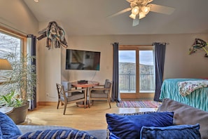 A cozy living room with a sofa, a TV, a dining table with chairs, and a balcony with a view.