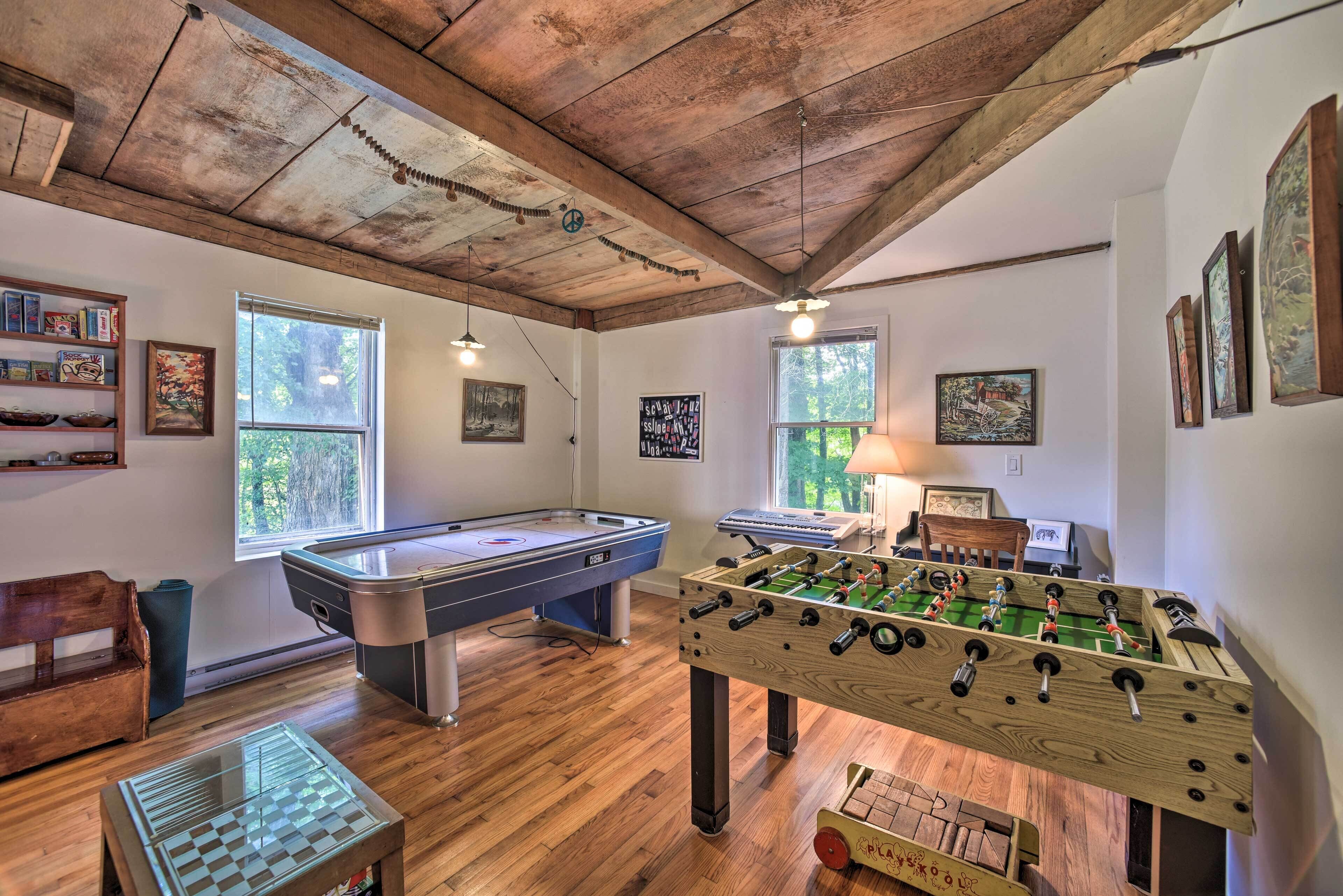 A room with a pool table, foosball table, and a foosball table in a rustic room with wooden beams and large windows.