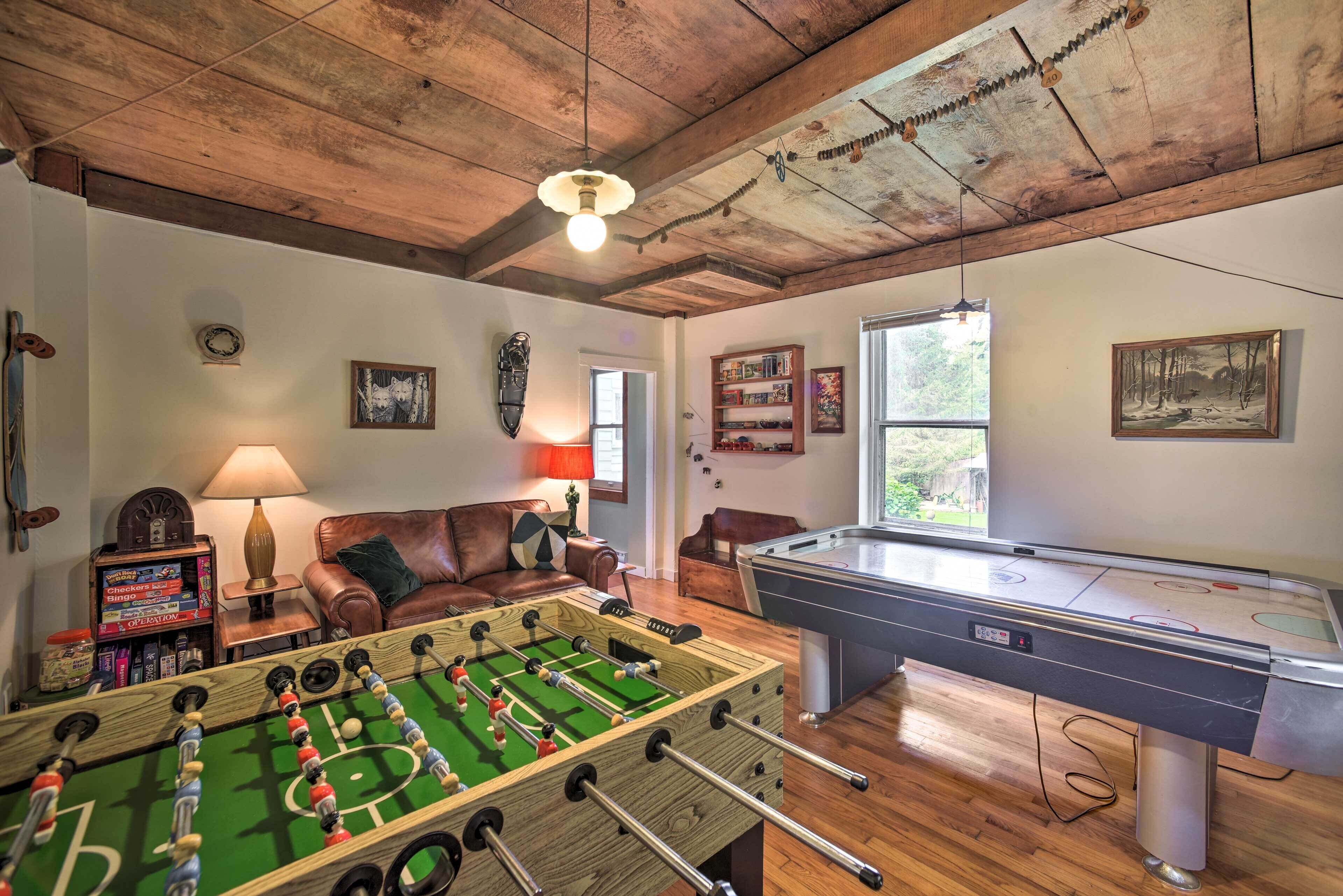 A cozy room with a foosball table, a pool table, a leather couch, and a lamp.