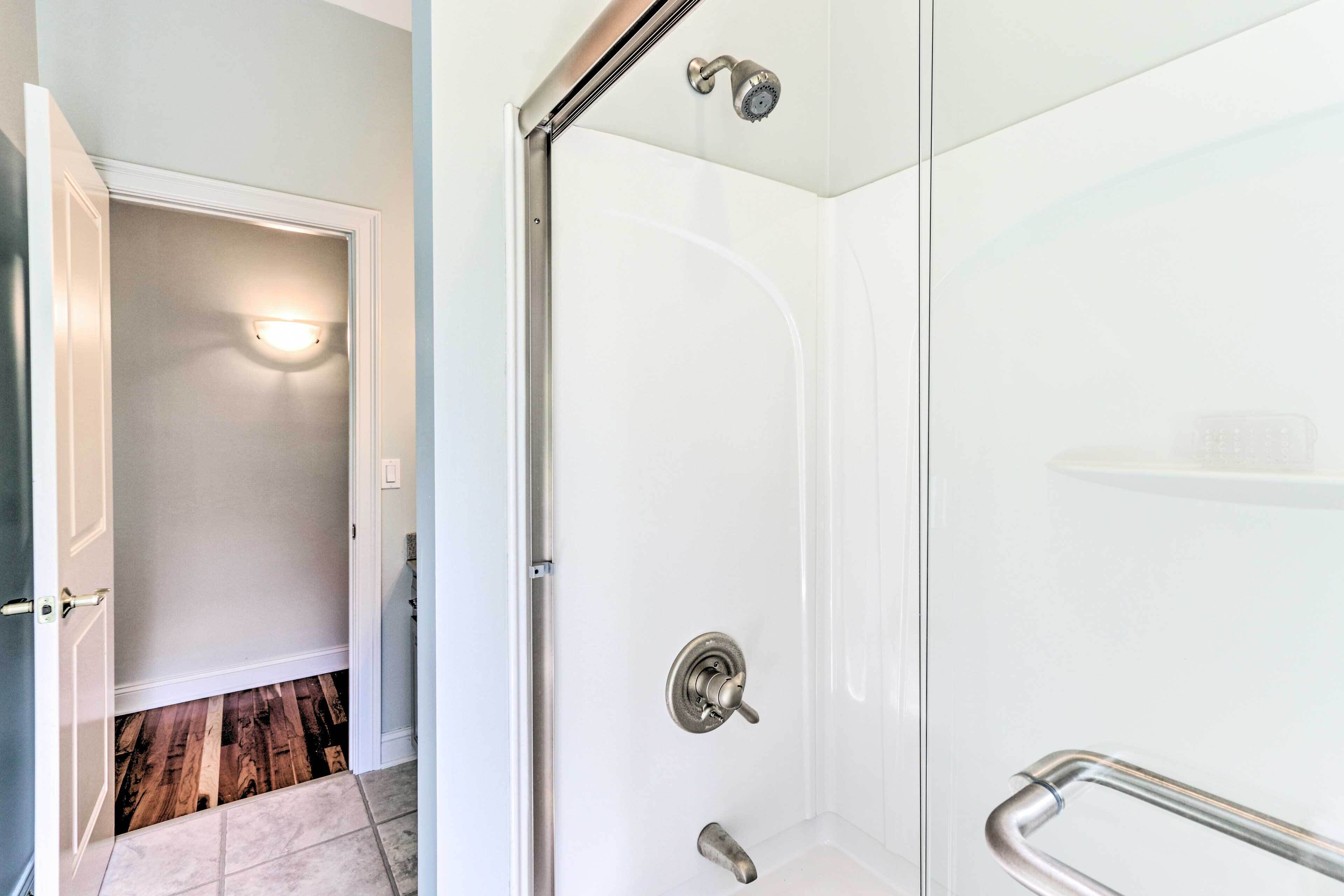 A modern bathroom with a glass shower enclosure, a white tiled floor, and a visible door leading to another room.