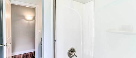 A modern bathroom with a glass shower enclosure, a white tiled floor, and a visible door leading to another room.