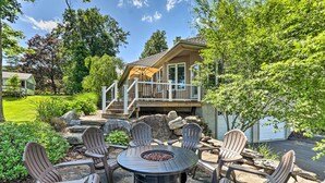 Eine Terrasse mit Adirondack-Stühlen und einer Feuerstelle, umgeben von einer Steinterrasse und Grünpflanzen.