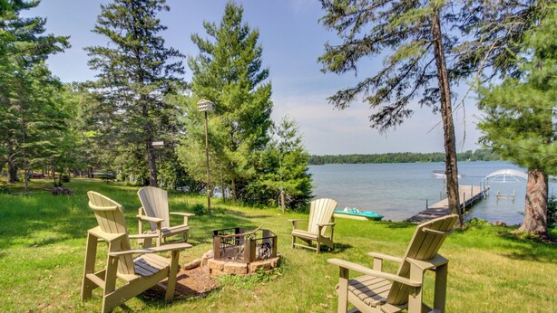Una location sul lago con poltrone Adirondack, un braciere e un molo che si protende sull'acqua.