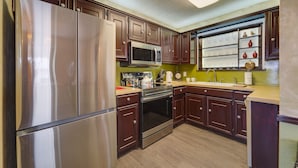 Una cocina con armarios de madera oscura, electrodomésticos de acero inoxidable, microondas y un lavabo.