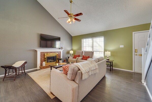 A living room with a fireplace, a sofa, a TV mounted on the wall, and a ceiling fan.
