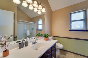 A modern bathroom with a white sink, two potted plants, a large mirror, and a window.