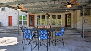 Une terrasse extérieure avec une table et des chaises, un ventilateur de plafond et un espace abrité avec des fenêtres.