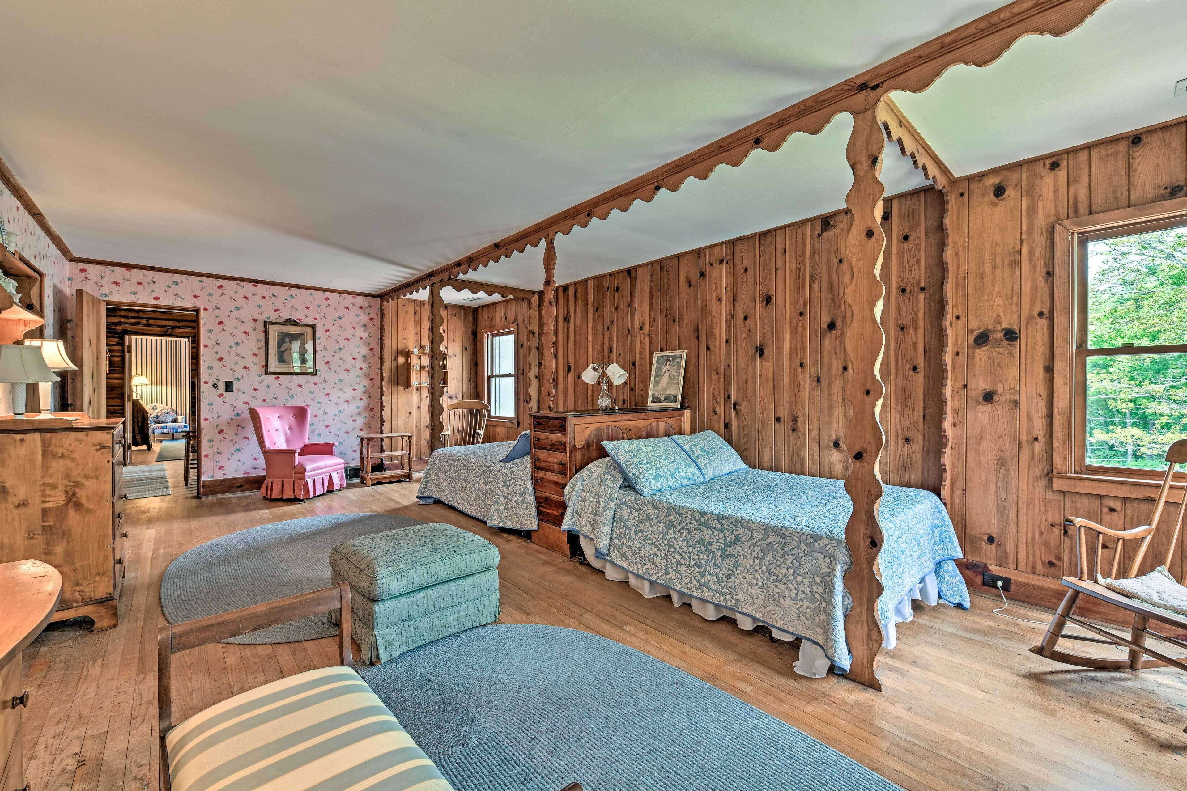 Una habitación acogedora de estilo cabaña con paredes de madera, dos camas con ropa de cama estampada, un sillón mecedor y una pequeña zona de escritorio.