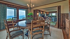 A dining area with a wooden table and chairs, a chandelier, and a view through large windows. - Amazing Historic Home w/ Stunning Mountain Views! (Blowing Rock)