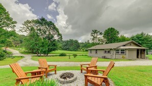 A cozy outdoor seating area with Adirondack chairs around a fire pit, a gravel path leading to a house, and a lush green landscape. - 2 Mi to Ski Sapphire: Pet-friendly Cashiers Cabin (Cashiers)