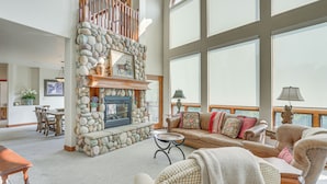 A spacious living room with a stone fireplace, a high ceiling, and large windows. - Expansive Edwards Condo on Main Street w/ Views! (Edwards)