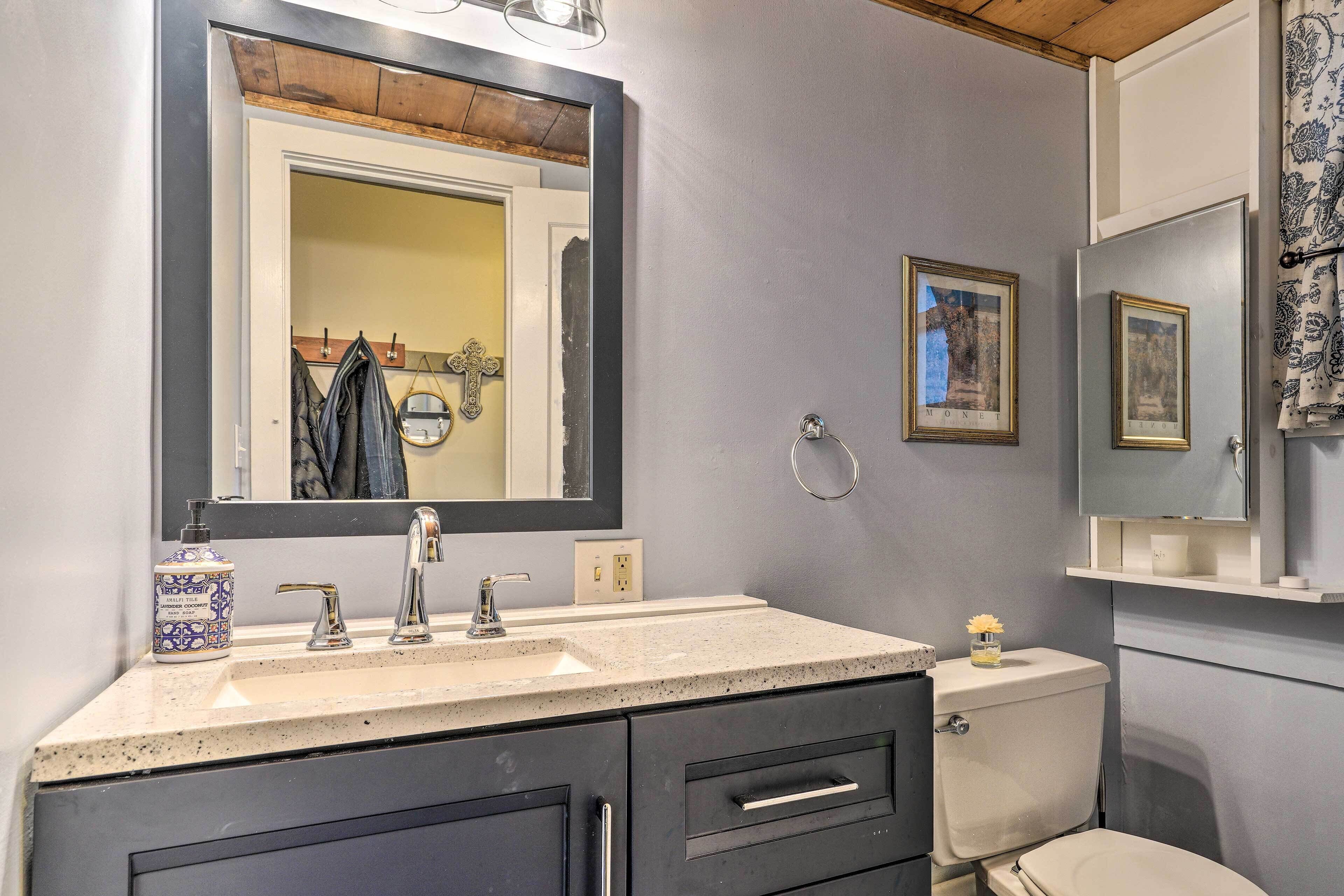 Une salle de bain avec un grand miroir, un lavabo à deux robinets, des toilettes et un meuble avec des tiroirs.