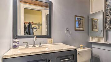 Une salle de bain avec un grand miroir, un lavabo à deux robinets, des toilettes et un meuble avec des tiroirs.