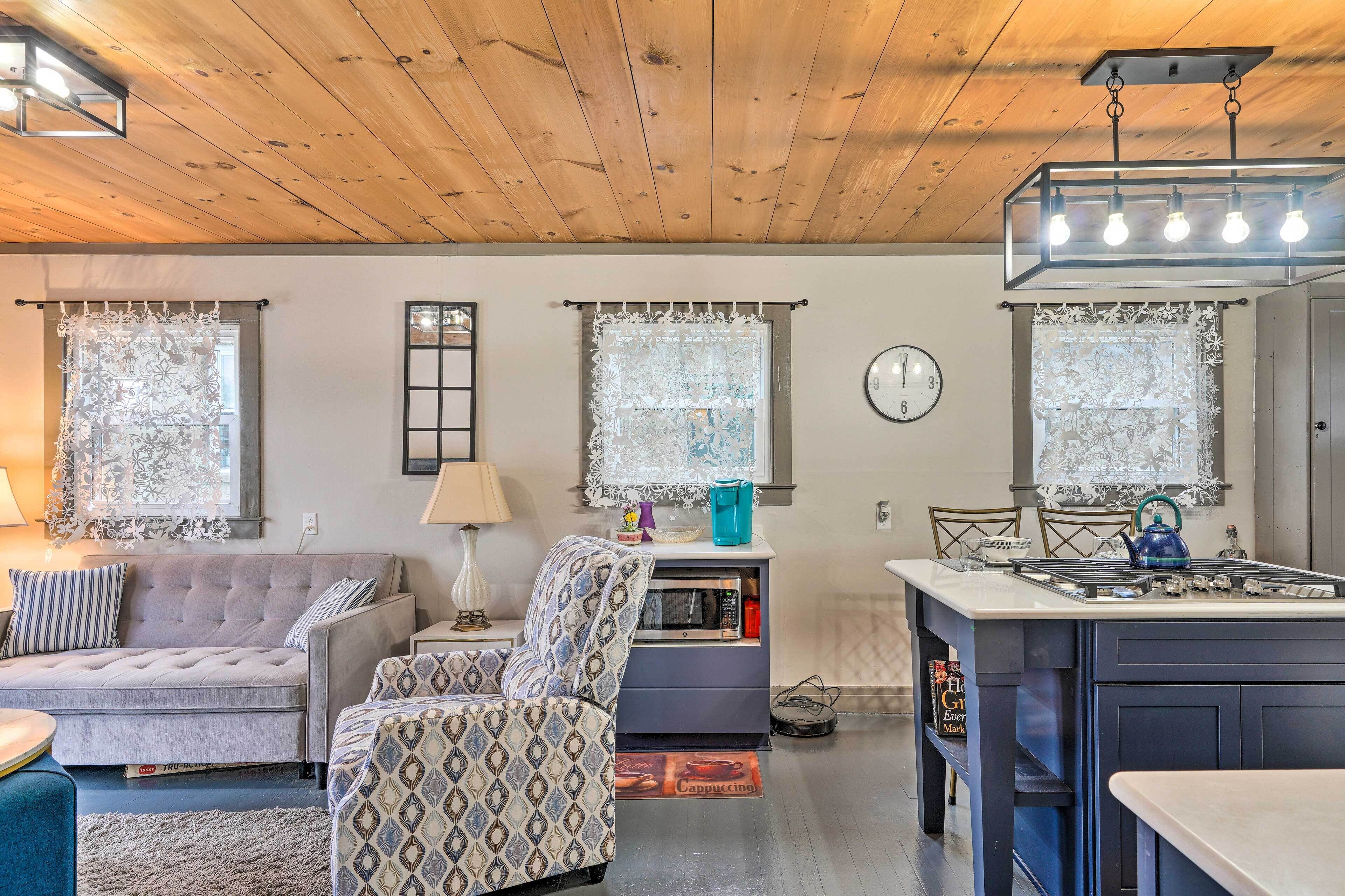 A cozy living room with a sofa, armchair, and a small kitchen area with a microwave and kettle.