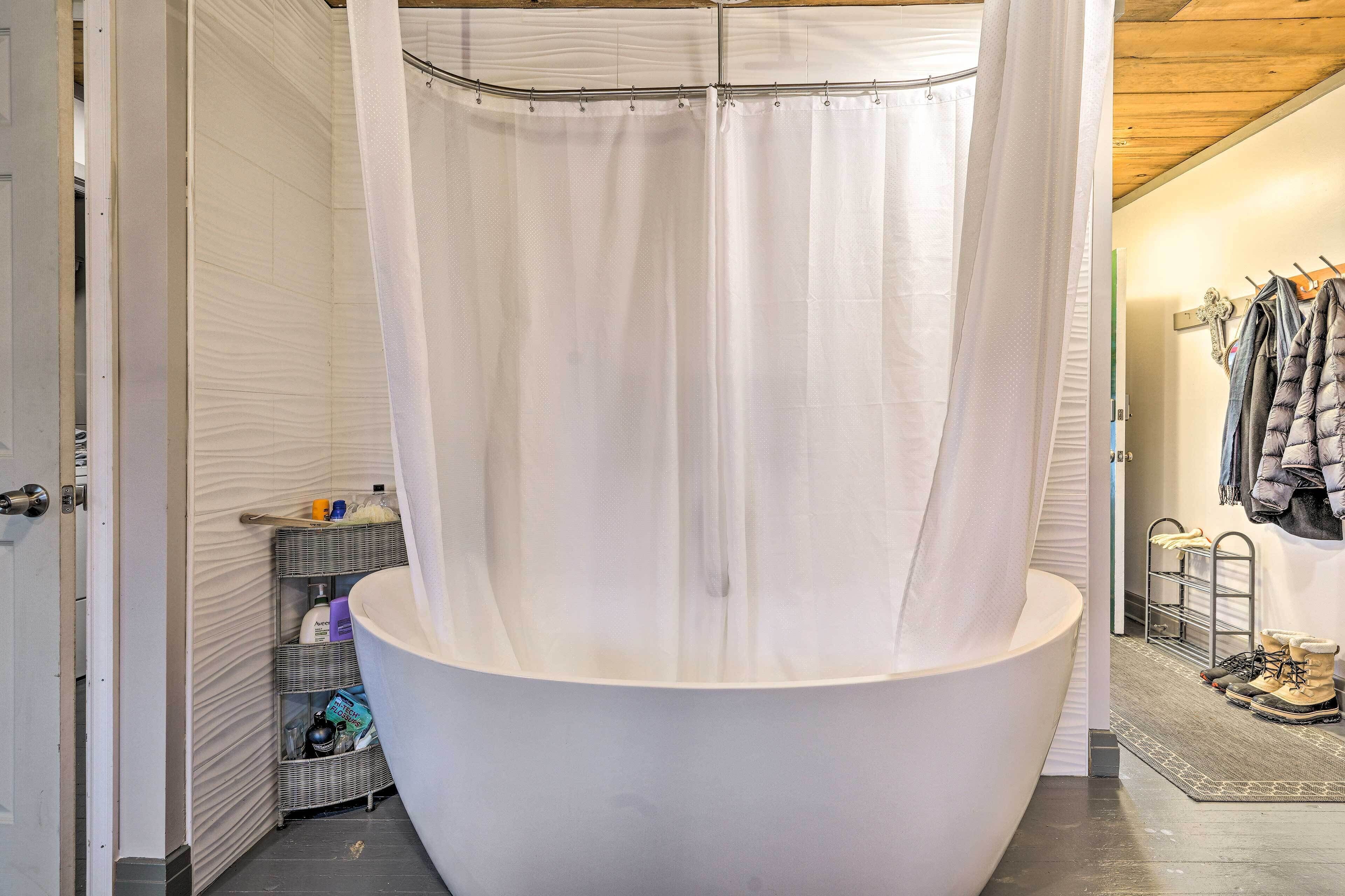 A bathroom with a large bathtub, a shower curtain, a wicker shelf with toiletries, and a rack with shoes.