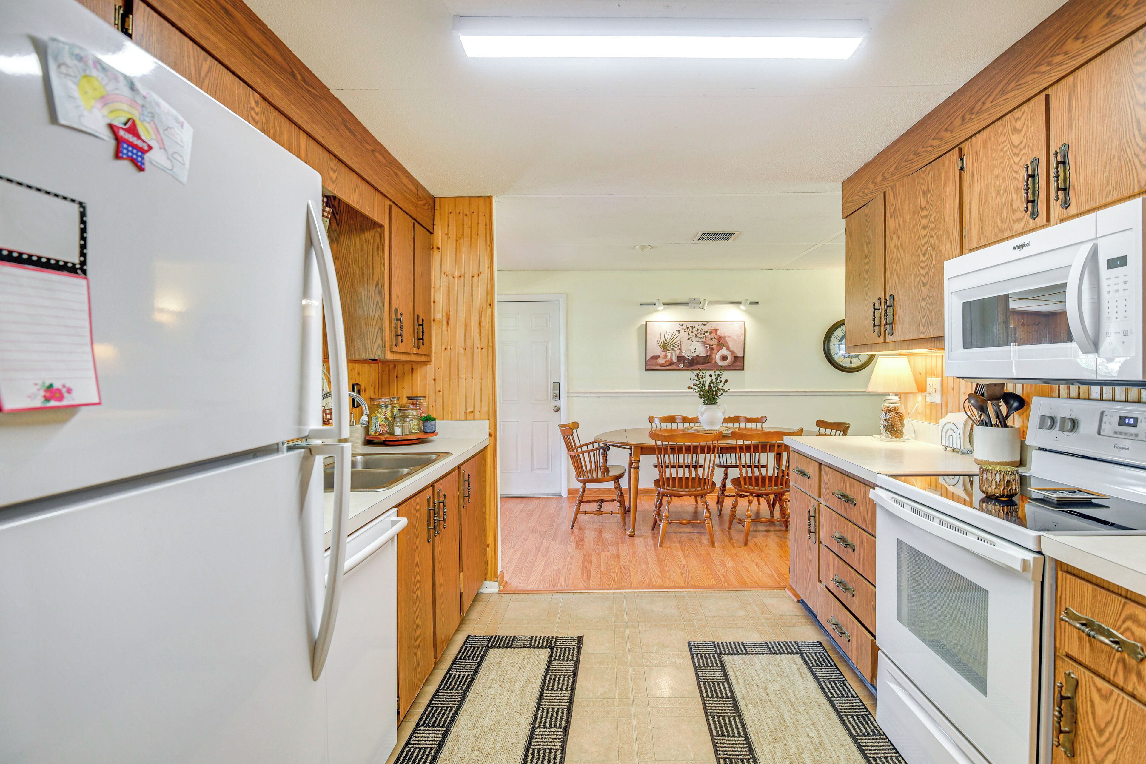 Una cocina con gabinetes de madera, un refrigerador, un microondas y una mesa de comedor con sillas.