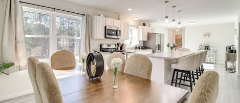 A modern kitchen with white cabinets, a central island, and a dining area with a wooden table and chairs.
