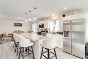 Cozinha moderna com armários brancos, eletrodomésticos de aço inoxidável e uma ilha central com banquetas.