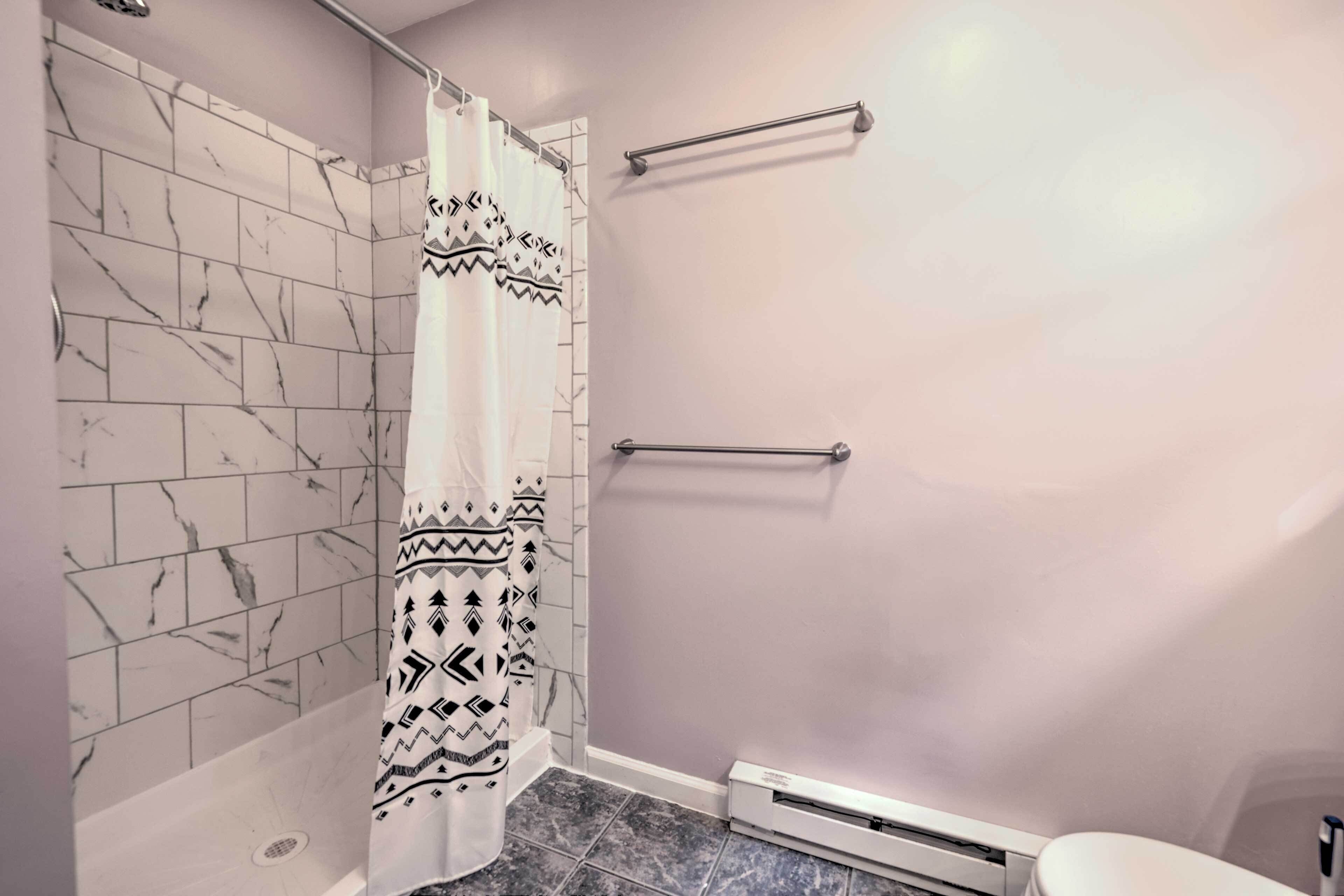 Un baño con ducha, azulejos de mármol, cortina de baño estampada y un toallero.