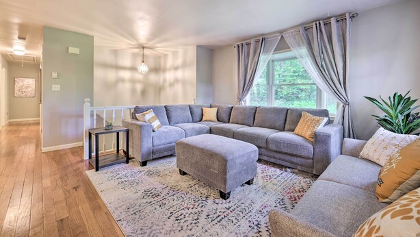 Un salon moderne avec un canapé d’angle, un pouf et un tapis à motifs.