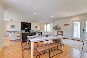 A spacious living area with a dining table set for six, a sofa, and a kitchen in the background.