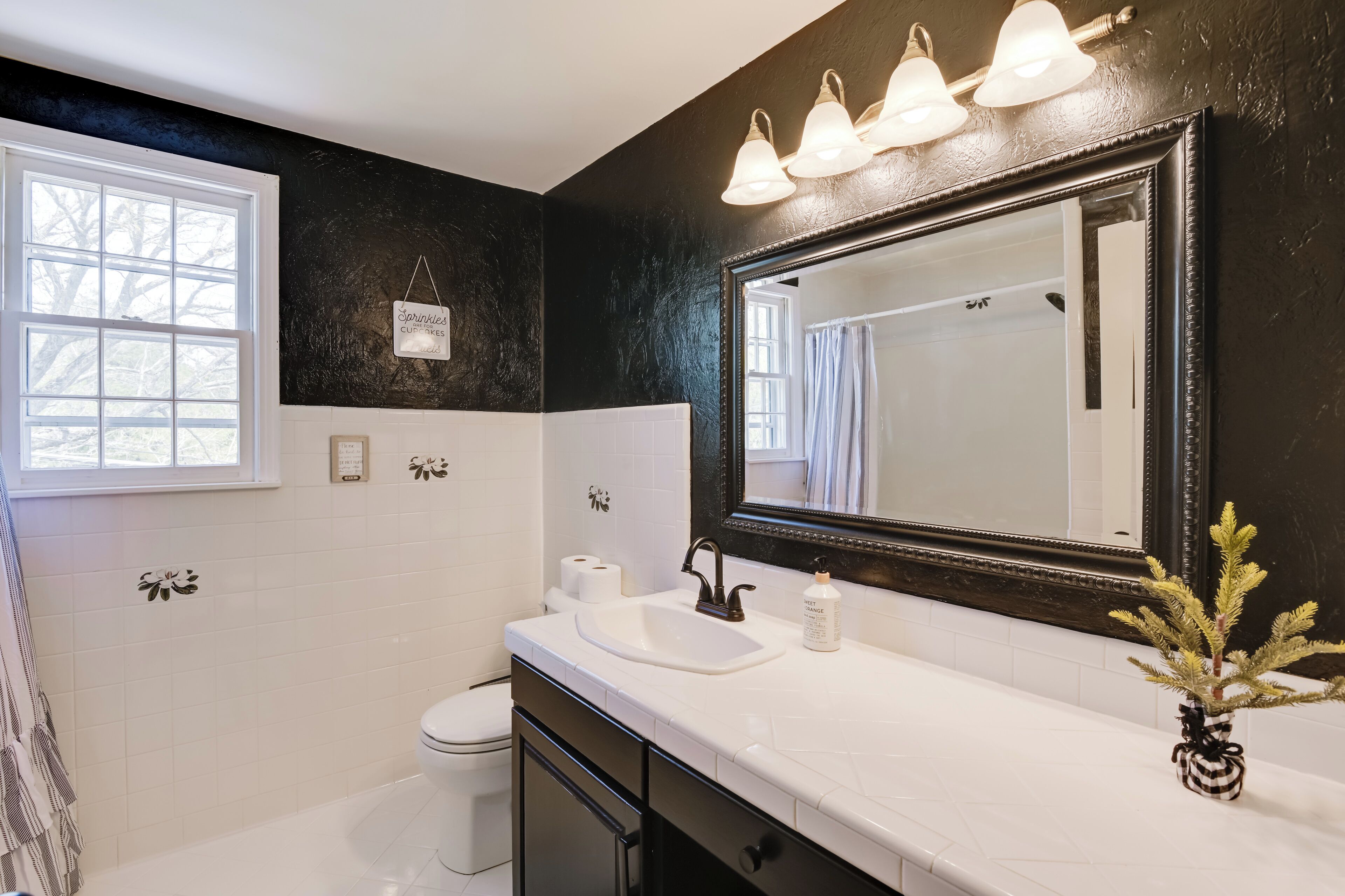 A bathroom with a white sink, black cabinets, a large mirror, and a window.