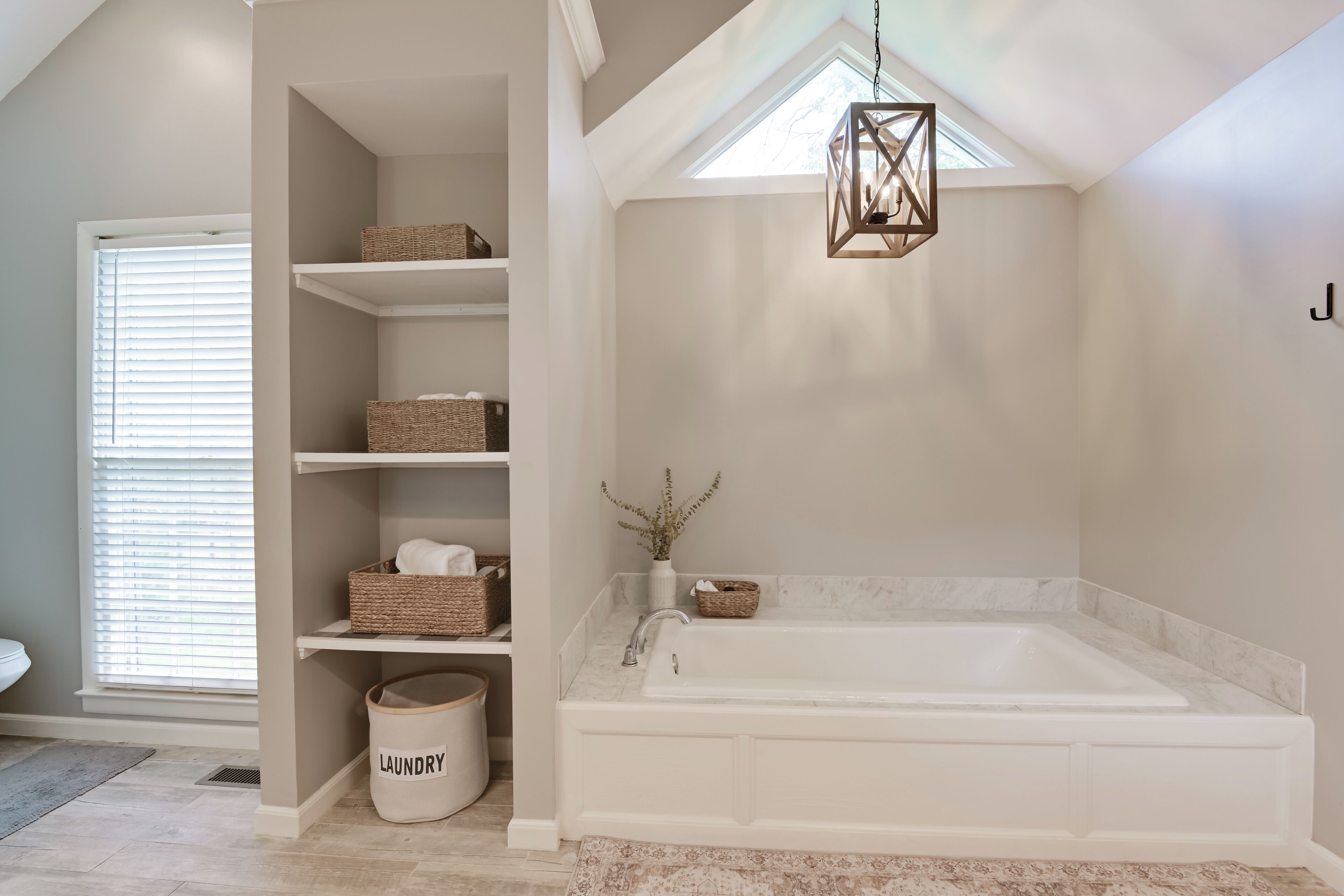 A bathroom with a freestanding bathtub, built-in shelves with baskets, a laundry basket labeled "LAUNDRY," and a hanging light fixture.