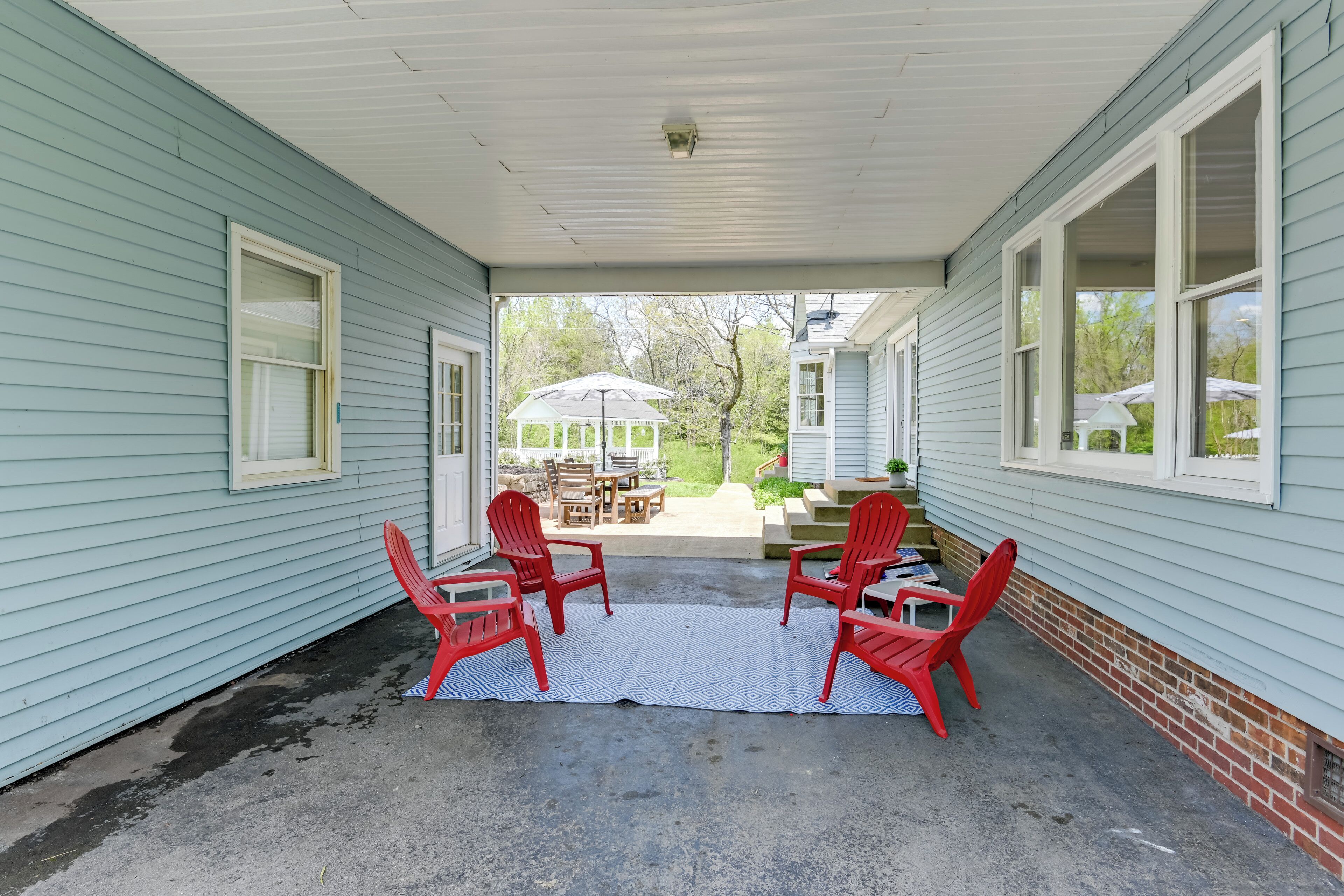 A covered porch with four red Adirondack chairs and a white rug.