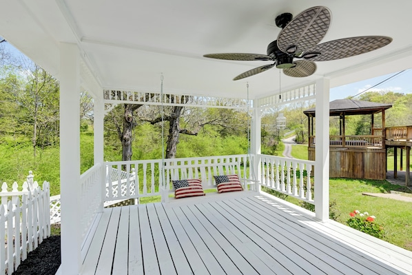 A white wooden porch with a ceiling fan, white picket fence, and two American flag pillows.