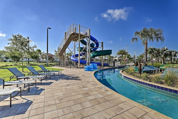 A pool area with a water slide, lounge chairs, and a clear blue sky.