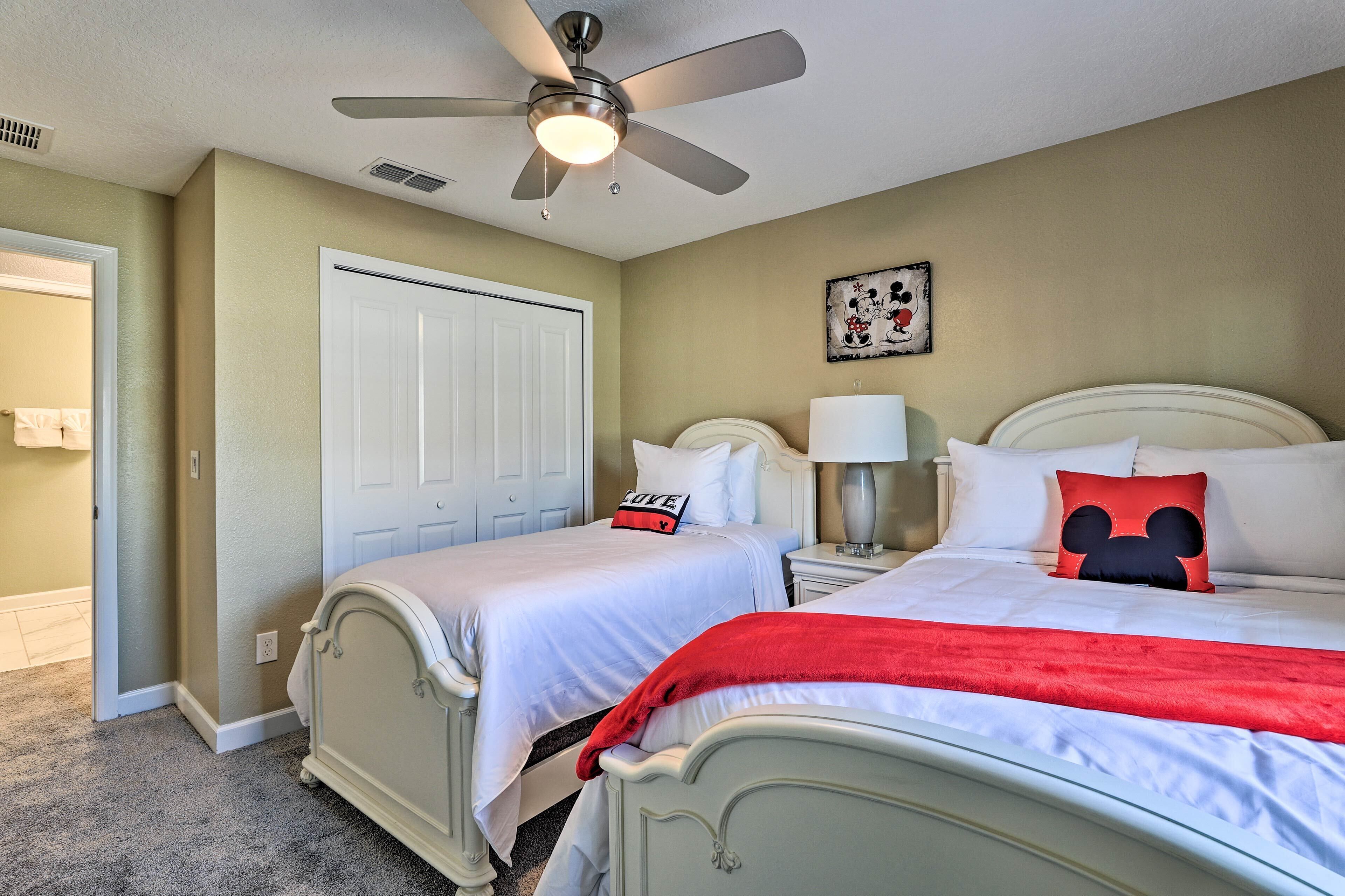 A bedroom with two beds, a ceiling fan, a door, a wall clock, and a Mickey Mouse pillow.