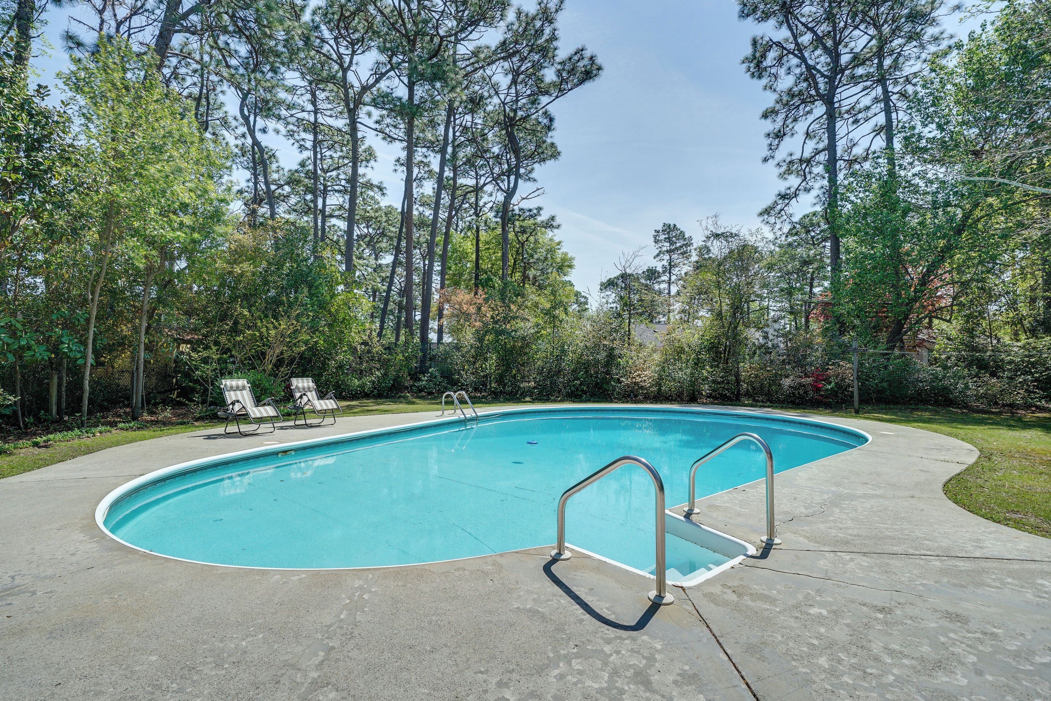 A swimming pool with a concrete deck, metal handrails, and two lounge chairs.