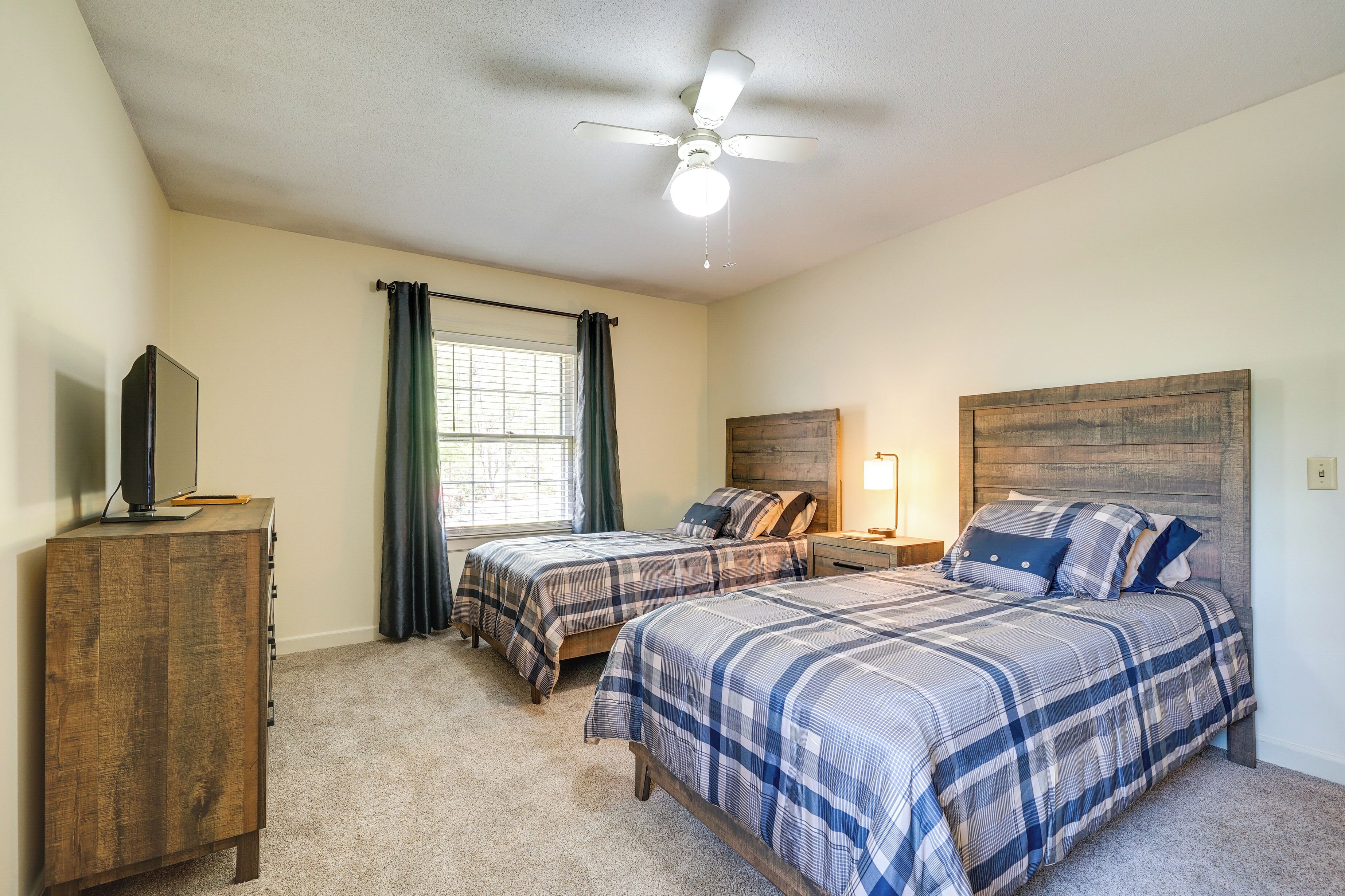 A bedroom with two beds, a ceiling fan, a TV on a wooden cabinet, and a window with curtains.