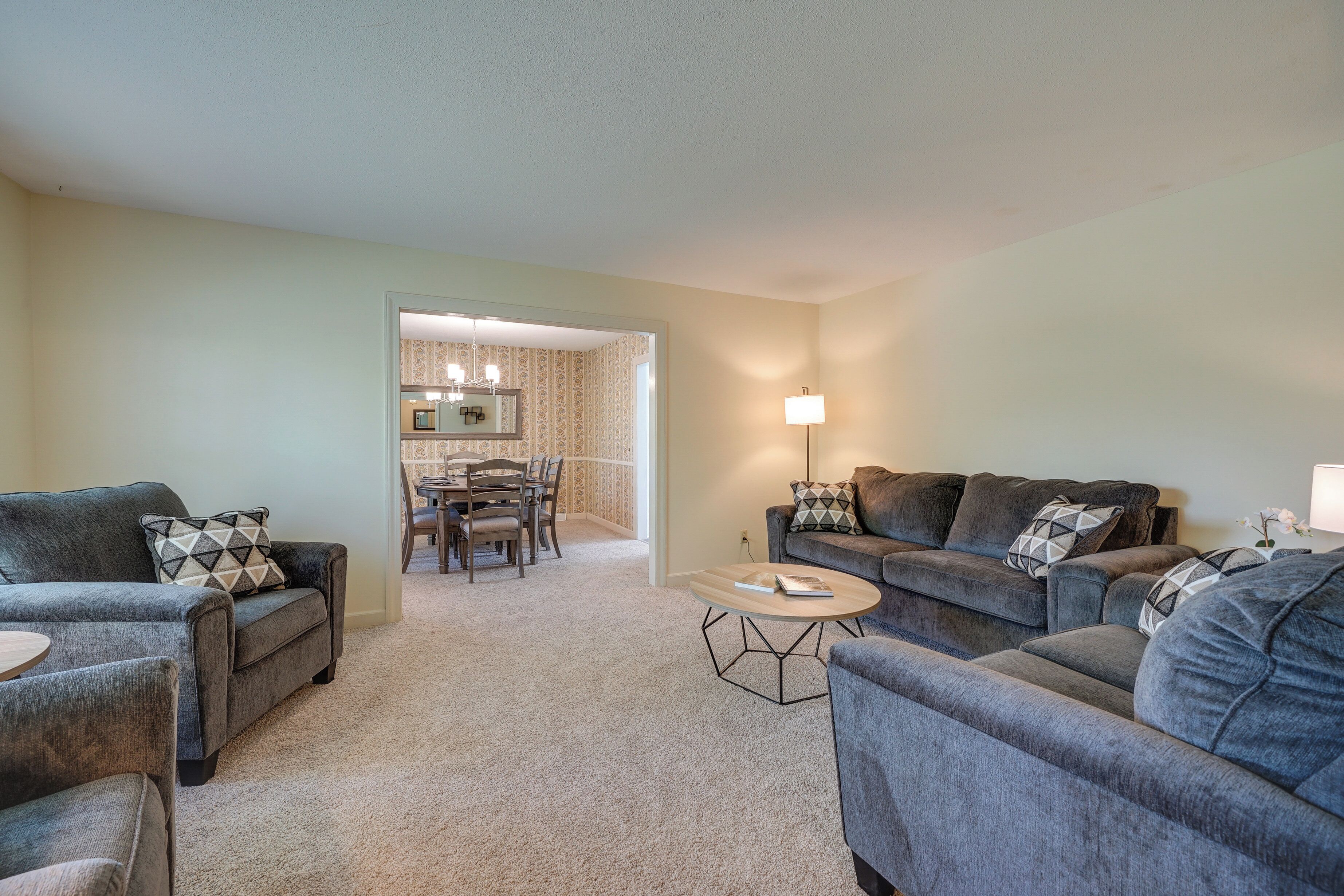 A living room with grey sofas, a coffee table, and a dining area with chairs and a table.