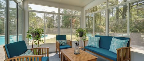 A sunroom with large windows, a pool, and outdoor seating.
