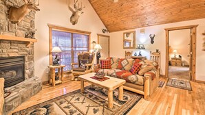 A cozy living room with a stone fireplace, wooden furniture, and deer antlers mounted on the wall. - Resort Perks! Woodsy Family Retreat Near SDC (Branson West)