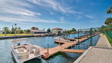 A marina with boats docked, a wooden dock, and a house in the background.