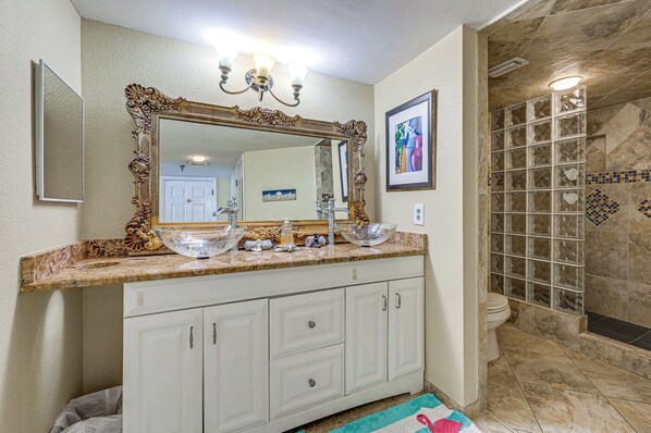 A bathroom with a large ornate mirror, a glass bowl sink, and a shower with a glass door. - On-site Beach Access! Waterfront Hudson Condo (Hudson)
