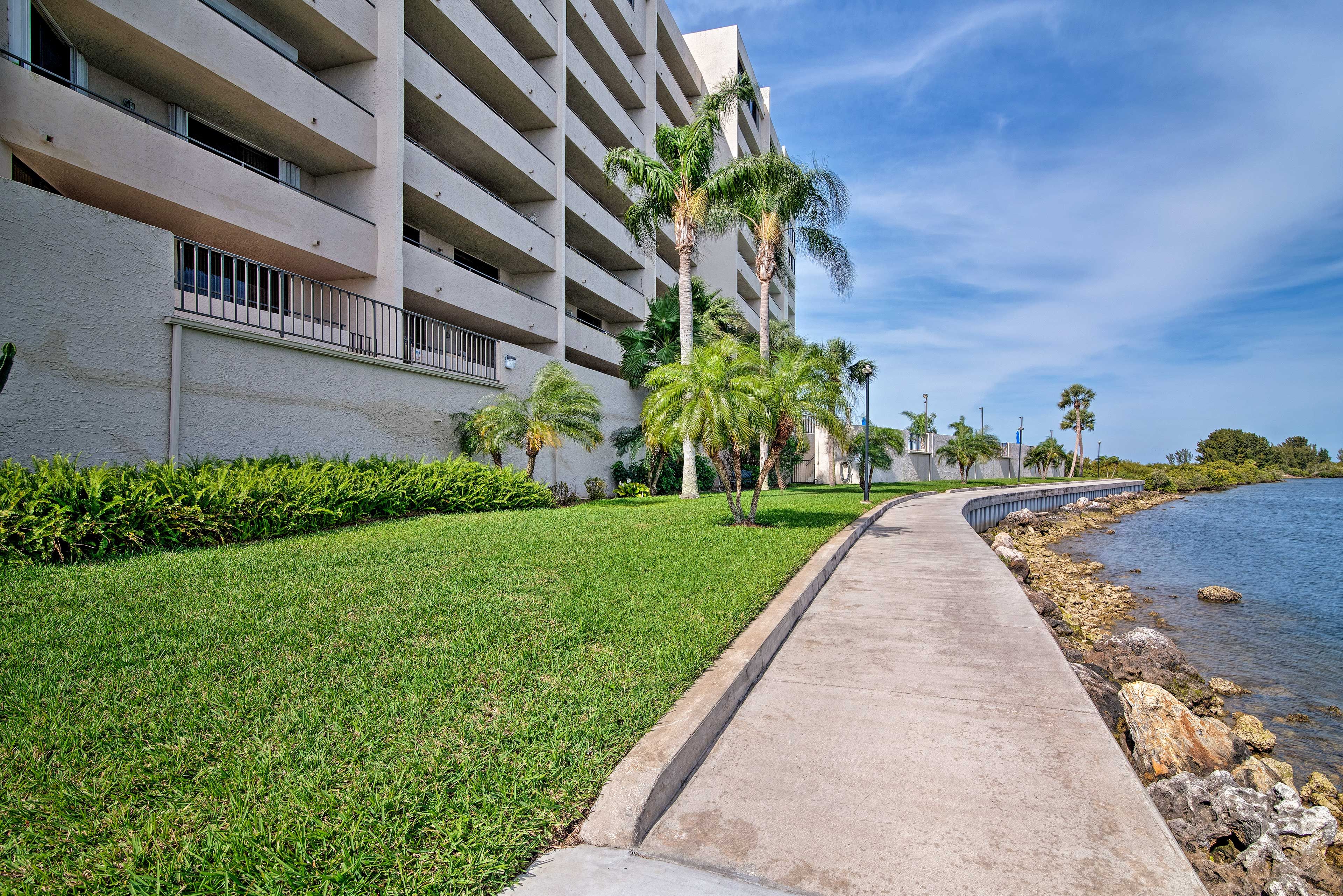 A beachfront hotel with a concrete walkway, palm trees, and a clear view of the ocean.