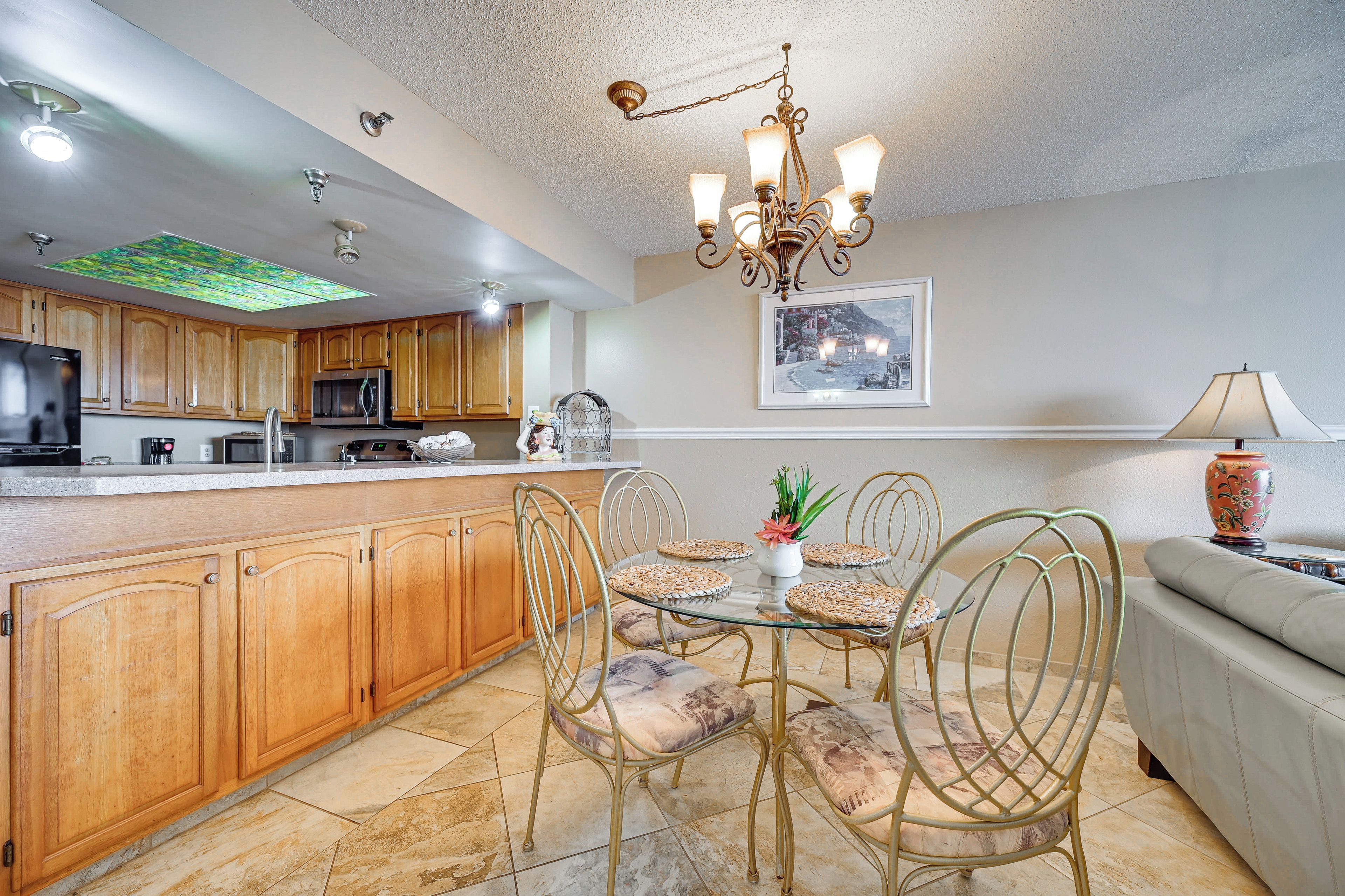 A kitchen with wooden cabinets, a stainless steel refrigerator, and a microwave. There is a dining area with a glass table and metal chairs.