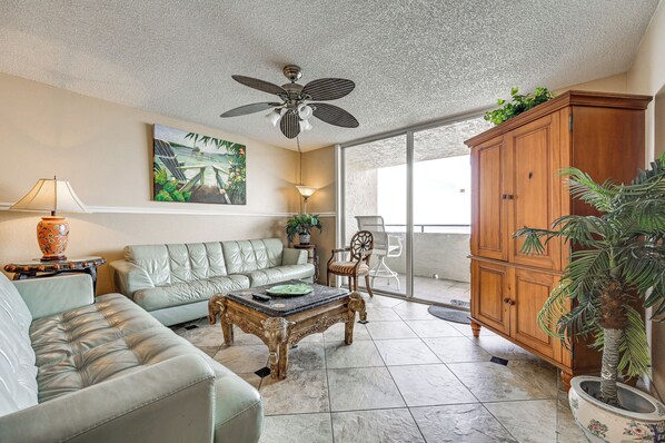 A living room with a sofa, a coffee table, a ceiling fan, a painting, and a wooden cabinet.