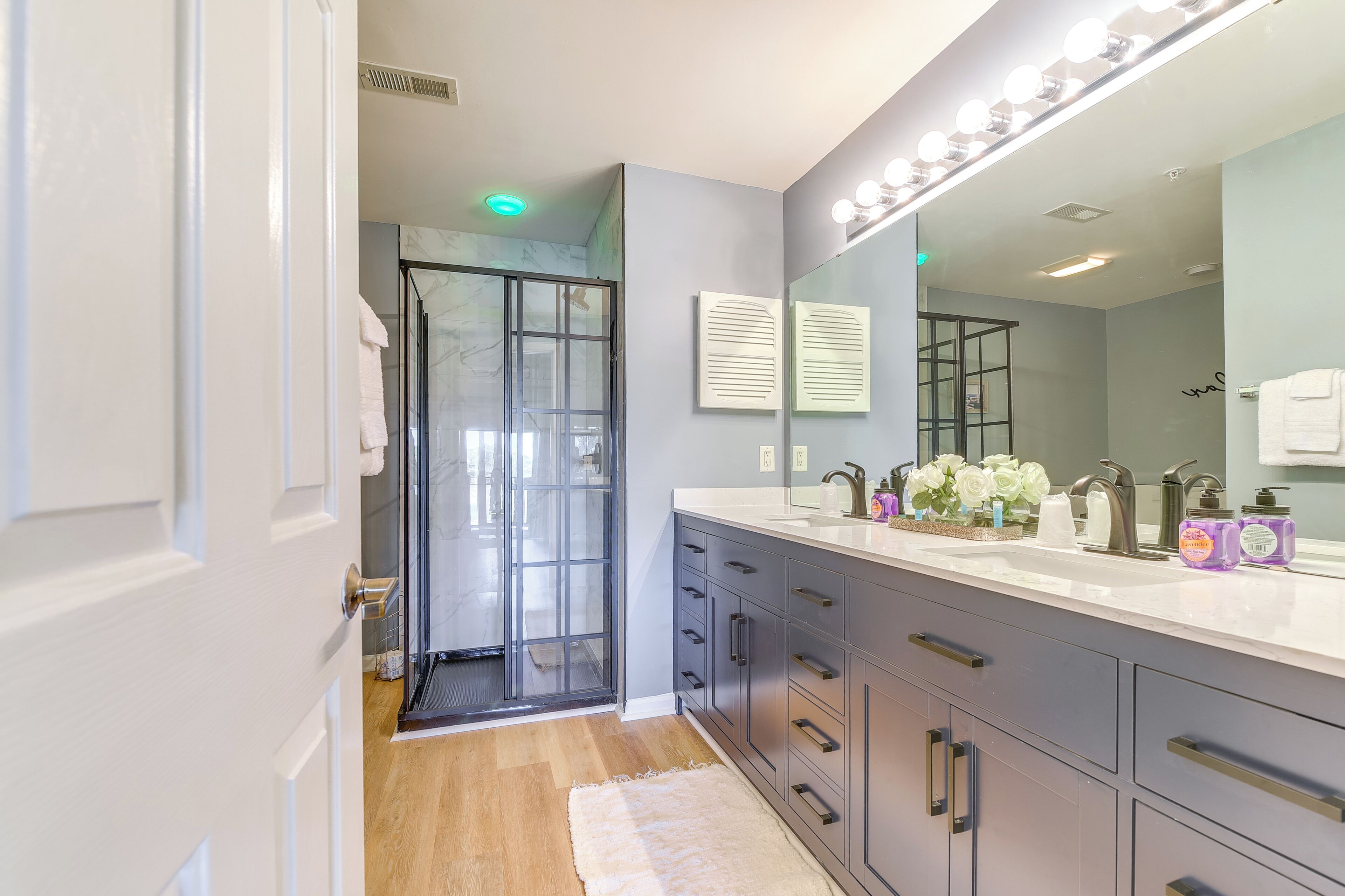 Une salle de bain moderne dotée d’une douche à parois de verre, d’un grand miroir avec éclairage intégré et d’un meuble-lavabo avec un évier et plusieurs tiroirs.