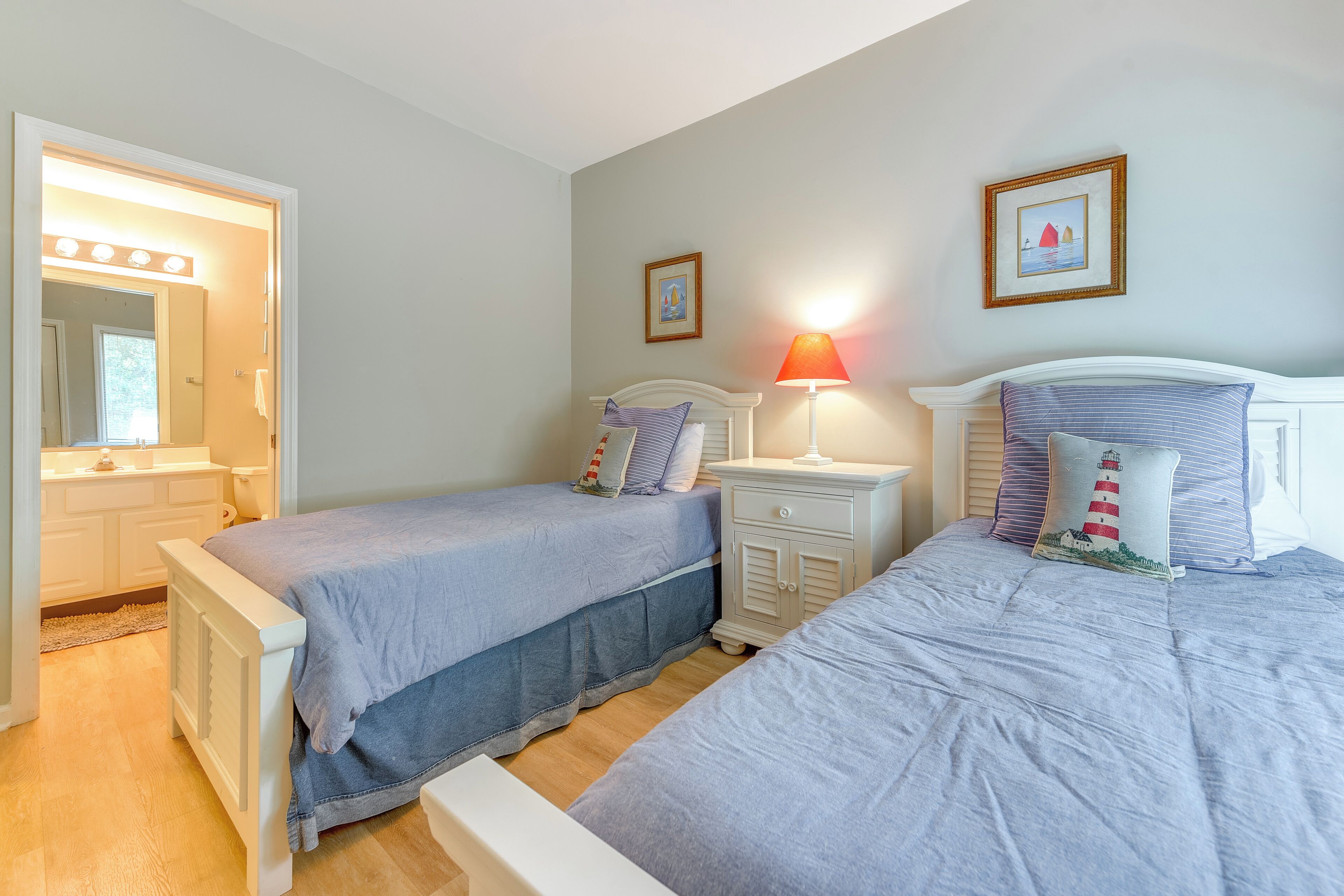 A bedroom with two beds, a nightstand with a lamp, a dresser, and a mirror with lights.