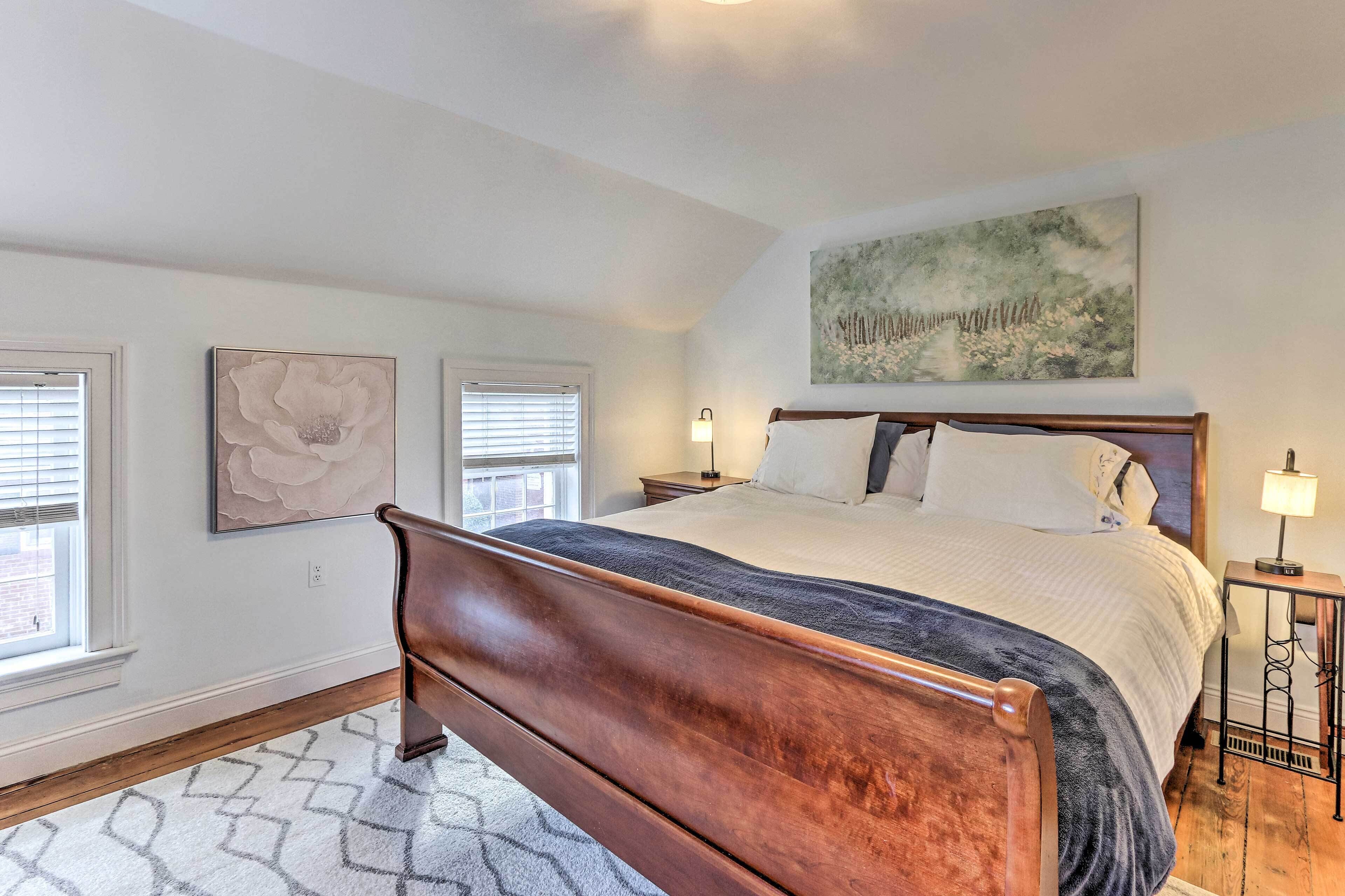 A bedroom with a wooden bed, a large painting on the wall, and a window with blinds.