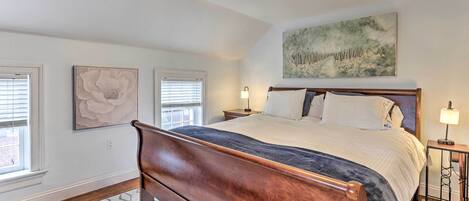 A bedroom with a wooden bed, a large painting on the wall, and a window with blinds.
